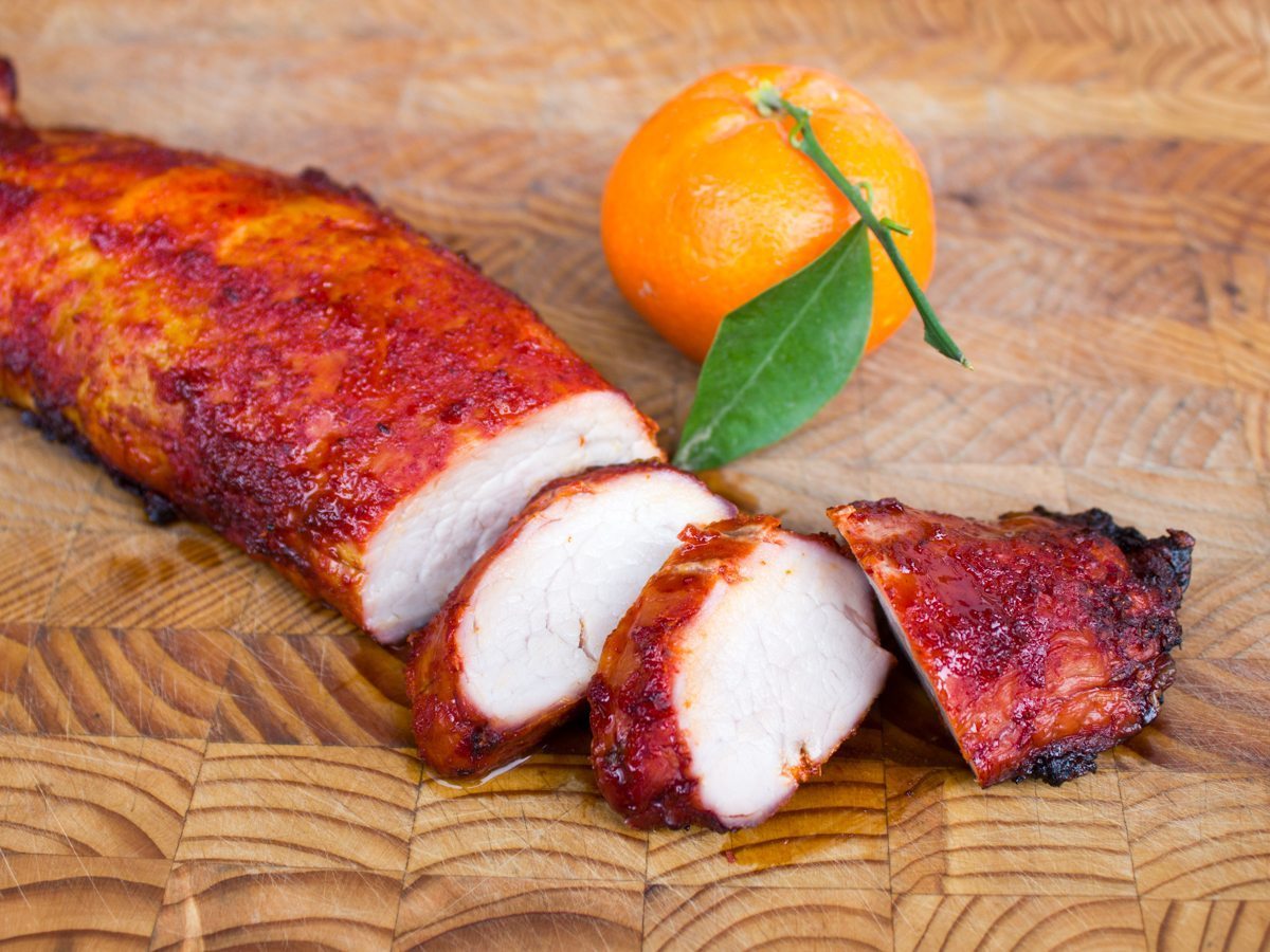 Sliced pork tenderloin and tangerine on cutting board